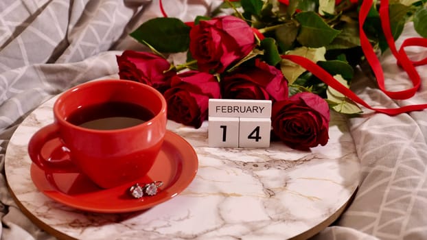 Background Festive Flatlay, composition for Valentine's Day on February 14. Coffee in a red cup, red rose flowers and diamond heart earrings at home in bed