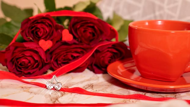 Background Festive Flatlay, composition for Valentine's Day on February 14. Coffee in a red cup, red rose flowers and diamond heart earrings at home in bed