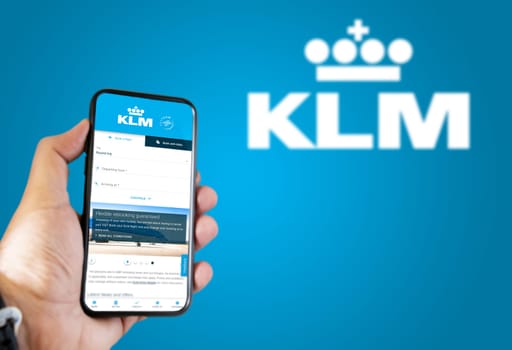 Amsterdam, NED, October 2021: Hand holding a phone with KLM Airlines flight booking application. KLM Airlines logo blurred on a blue background. Booking airline tickets