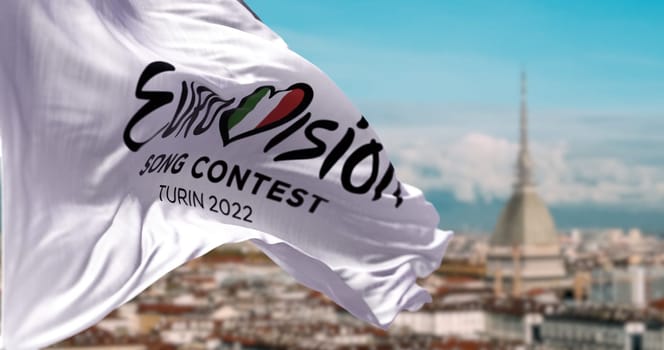 Turin, Italy, January 2022: the white flag with the Eurovision Song Contest 2022 logo waving in the wind with blurred landscape of Turin. The 2022 edition will take place in Italy from 10 to 14 May