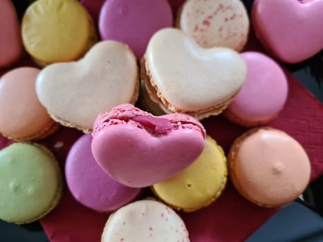 Top view of three delicious macarons and love heart symbol on napkin on wooden table. Romantic vintage valentines day and wedding background