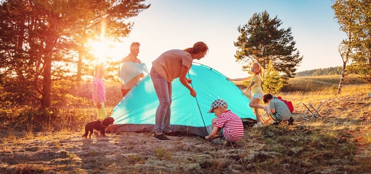 Groupof the people setting up the tent on the nature near the sea. Concept of the family hiking and children's scout camping.