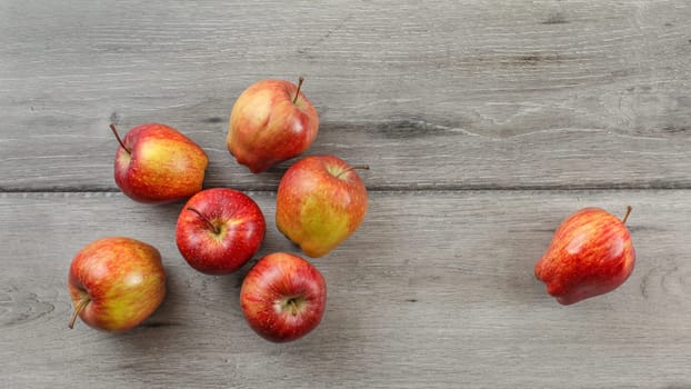 Tabletop view, 7 red glossy apples on gray wooden desk.
