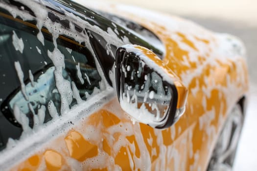Detail on yellow car side mirror, covered with shampoo and foam spots, when washed in carwash.