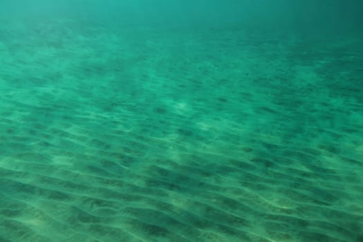 Sea bottom, small "dunes"" in sand lit by sun shining from above. Abstract marine background."