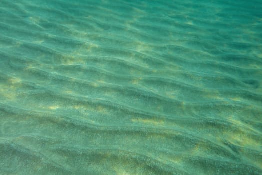Sea bottom underwater photo, "dunes"" in sand lit by sunlight. Abstract marine background."