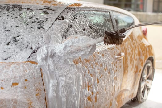 Yellow car washed in self service carwash. Shampoo  spraying to side mirror, already covered in white foam, drops spraying everywhere.