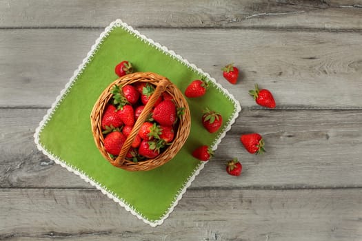 Tabletop view, small basket full of strawberries, some of them spilled on green table cloth under it.