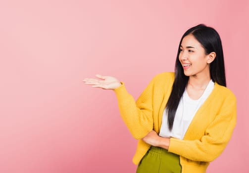 Asian happy portrait beautiful cute young woman smile standing presenting product holding something on palm away side, studio shot isolated on pink background with copy space, female show hand gesture