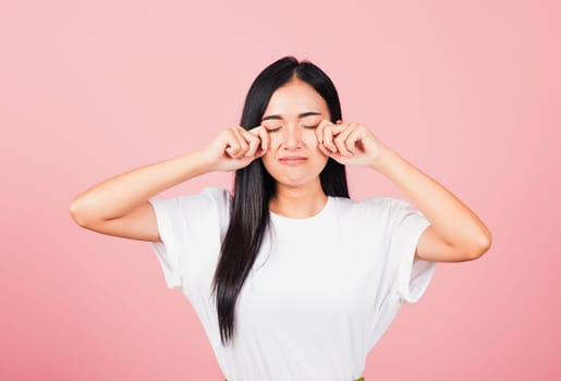 Asian portrait beautiful cute young woman bad mood her cry wipe tears with fingers, studio shot isolated on pink background, Thai female feeling sad unhappy crying with copy space