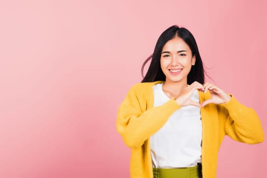 Happy Asian portrait beautiful cute young woman smile make finger heart gesture figure symbol shape sign with two hands sending love to her lover looking camera, studio shot isolated pink background