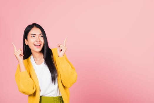 Asian happy portrait beautiful cute young woman standing makes gesture two fingers point upwards above presenting product something, studio shot isolated on pink background with copy space