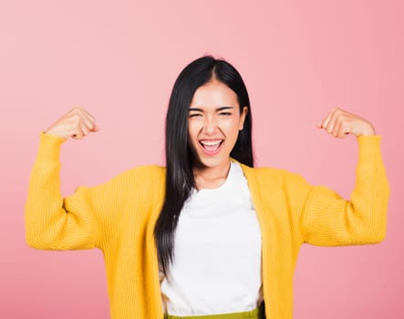 Portrait Asian of happy beautiful strong muscles young woman raises arms biceps confident showing power and strength have feeling independent victory successful, studio shot isolated pink background