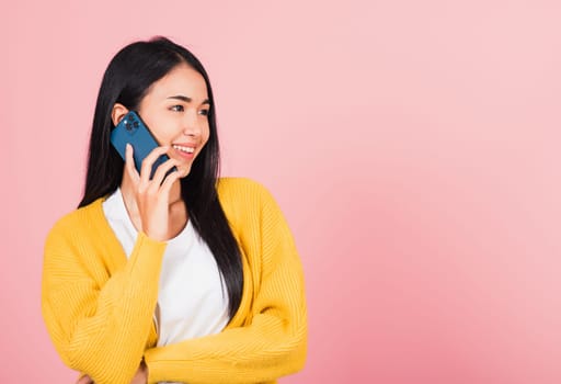 Portrait Asian happy beautiful young woman smile talking by smartphone looking to side away isolated, studio shot isolated on pink background, Thai female hold the phone to calling with copy space