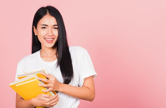 Portrait of beautiful Asian young woman teenage smiling hugging books, female person holding book multicolor, studio shot isolated on pink background with copy space, education concept