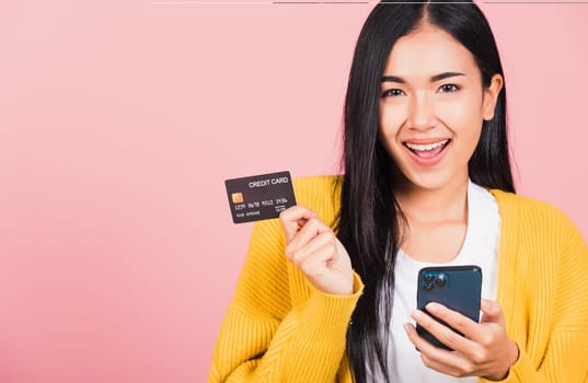 Happy Asian portrait beautiful cute young woman excited smiling hold mobile phone and plastic debit credit bank card, studio shot isolated on pink background, female using smartphone online shopping