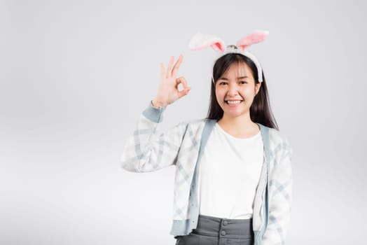 Easter day concept. Smiling happy woman wearing rabbit ears show OK finger sign, studio shot isolated on white background with copy space