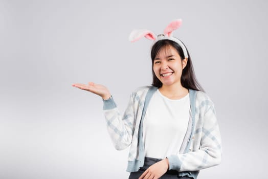Easter day concept. Smiling happy woman wearing rabbit ears presenting product holding something on palm away side, studio shot isolated on white background with copy space