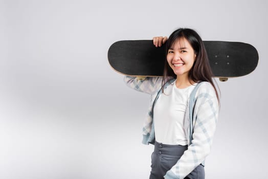 Smiling happy woman holding skateboard on shoulder, Happy Asian beautiful young female excited hold hands longboard, studio shot isolated on white background with copy space, sport extreme