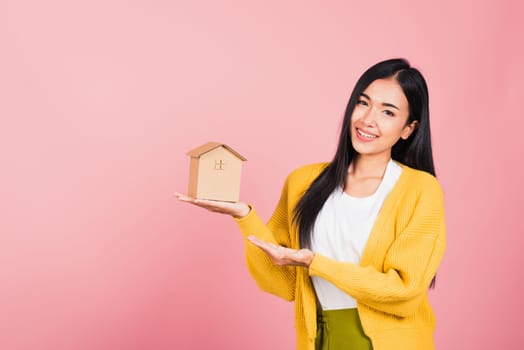 Happy Asian portrait beautiful cute young woman excited smiling holding house model on hand, studio shot isolated on pink background, broker female hold home real estate insurance and banking concept
