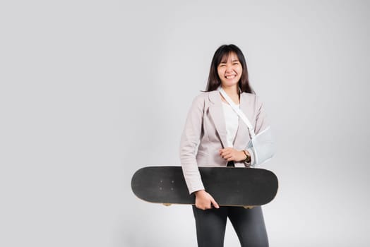 Woman smile broken arm after accident wear arm splint for treatment she play skateboard skating accident sport extreme, happy Asian female sling support hand isolated on white background, copy space