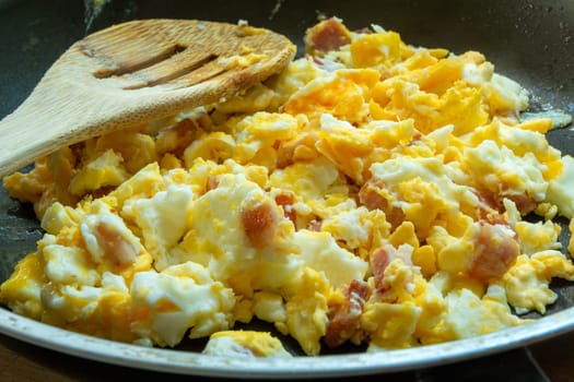 Scrambled eggs with bacon in a pan, close up
