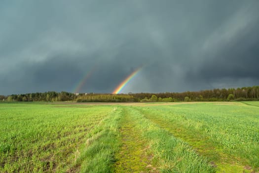 Cloudy sky with a fragment of a rainbow and a green meadow, Czulczyce, Poland