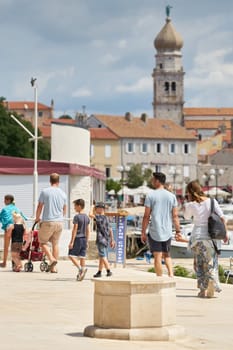 Holidaymakers on the promenade in the harbor in front of the old town of Krk on the Adriatic Sea in Croatia in summer