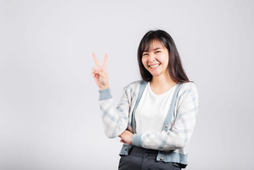 Woman showing finger making v-sign victory symbol side away looking to camera, Happy Asian beautiful young female mark peace gesture symbol, studio shot isolated on white background with copy space