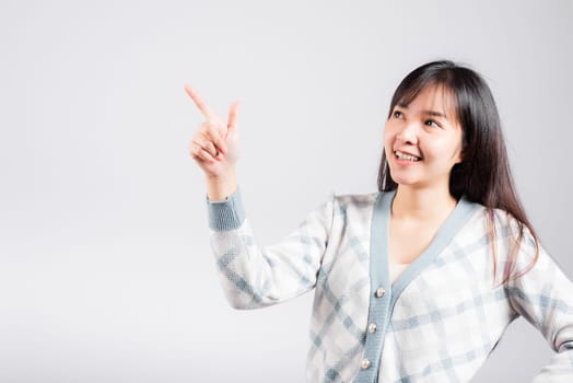 Smiling happy woman pointing finger out space, Portrait Asian beautiful young female point into empty looking to side away, studio shot isolated on white background with copy space