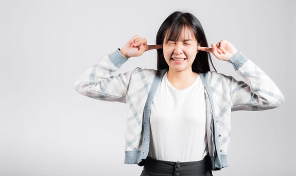 Woman bad mood pain her closed ears with finger and close eyes, Asian beautiful young female covers ears for loud noise, studio shot isolated on white background with copy space