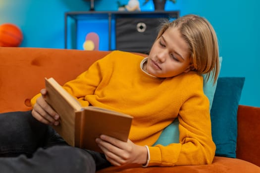 Caucasian teenager boy enjoys reading a book at home. Enthusiastically flips through pages, occasionally looking thoughtfully while lying comfortably on sofa, showing concentration and enjoyment