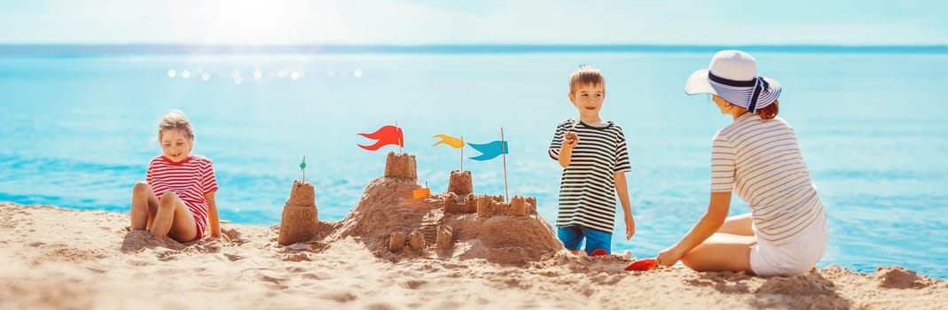 Mother with son and daughter sitting on the beach and building a sand castle. Concept of the family vacation.