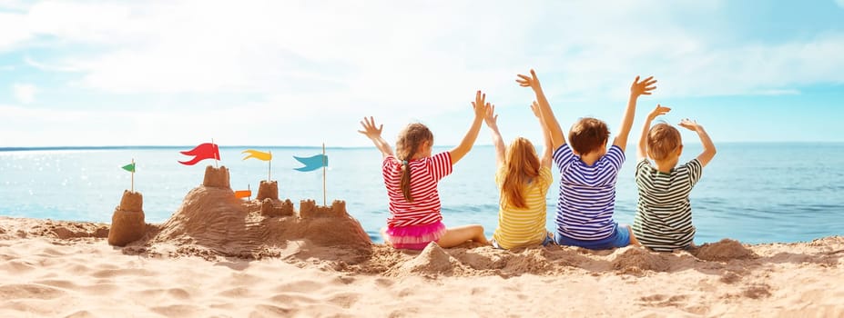 Four happy children sitting onthe sea coast and raising up their hands. Concept of the friendship and vacation.