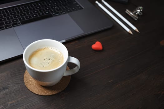 Coffee pause concept. Coffee cup, laptop, heart-shaped eraser and pencils on wooden background. Selective focus.