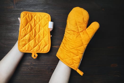 Yellow cooking mitten and potholder for hot dishes in female hands. Kitchen utensils.