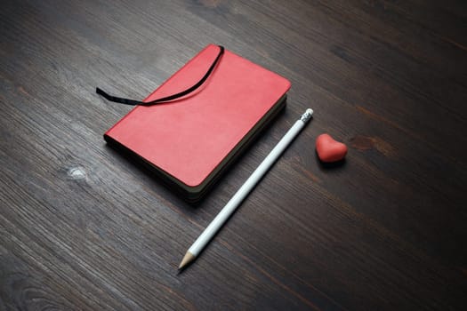 Blank red notepad, pencil and heart-shaped eraser on wooden background. Template for placing your design.