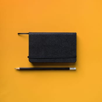 Photo of blank black notepad and pencil on yellow background. Responsive design template. Flat lay.