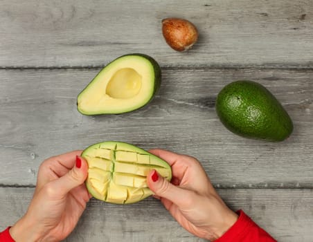 Tabletop view on woman hands preparing avocado, getting out the pulp cut in squares.