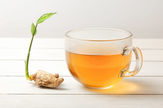 Cup of ginger tea (hot steam and moisture drops on glass), dry root with green spring next to it.