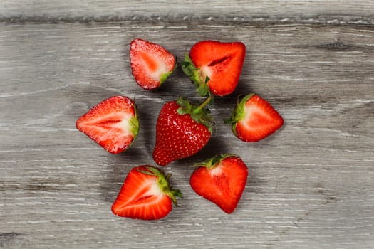Tabletop view - whole strawberry with halves around, forming circle, on gray wood desk.