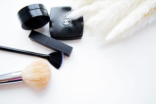 Moscow, 2021. Lipstick, brushes and blush lie together next to fluffy branch of the cane on white background with place for text. High quality photo