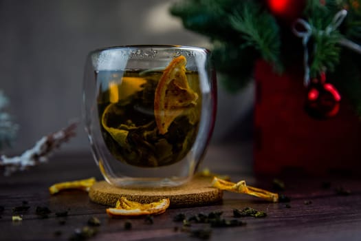 A transparent cup of tea stands on a dark table, on a wooden stand, dried orange slices float in the cup, citrus slices lie next to it, tea is scattered, a photo in a dark key. High quality photo