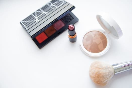 Moscow, 2021. The white face powder and bronzer, black packaging with eye shadow, lipstick and brush lying on white background. High quality photo