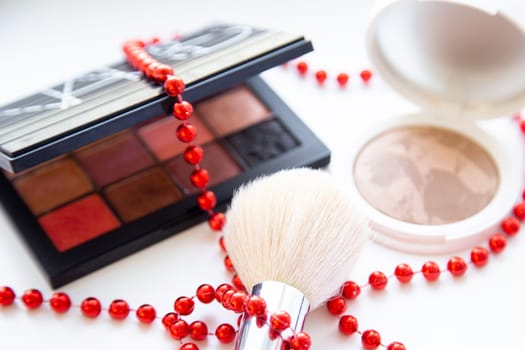 The white face powder and bronzer, black packaging with a eyeshadow brush and lying on a white background, braid with red beads closeup. High quality photo