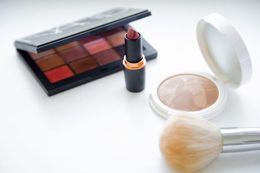The white face powder and bronzer, black packaging with eye shadow, lipstick and brush lying on white background. High quality photo