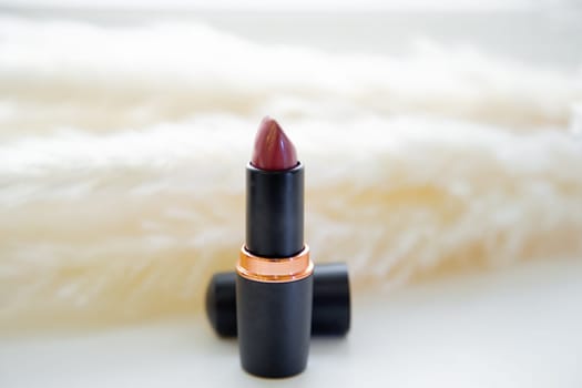 Open red lipstick stands on the background of fluffy reeds on a white background. High quality photo