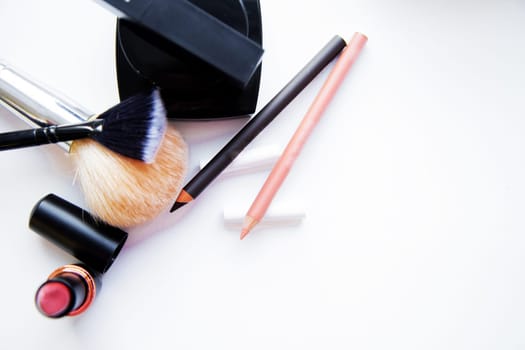 Two pencils for eyes and lips, lipstick, brushes and blush lie together on a white background with a place for text. High quality photo
