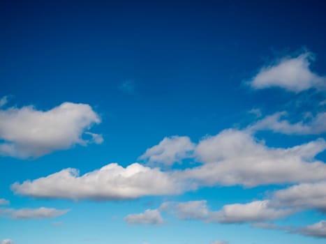 Full-frame view of a blue sky with a light-dark gradient and isolated white clouds.