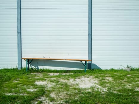 Single foldable beer tent bench on a lawn on a lightweight wall.